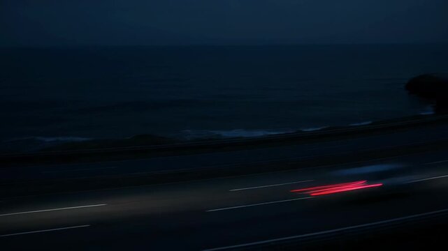 Dark highway by the sea at night with car light streaks