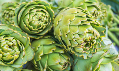 Fototapeta premium Close-up of pile fresh organic green artichokes, unique scale-like texture and vibrant color of globe artichokes, ideal for healthy eating and Mediterranean diet concepts.