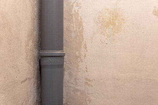 Gray plastic pipe near a dirty plastered wall