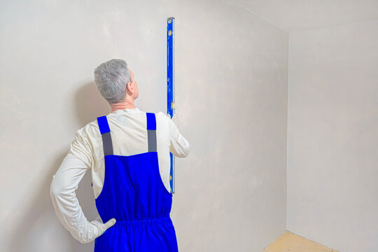 The builder checks the verticality of the plastered surface