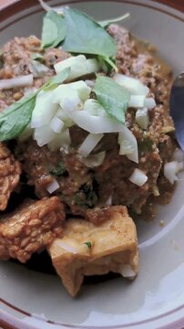 A cinematic close-up shot of traditional Indonesian dish Nasi Pecel, featuring fresh vegetables and rich peanut sauce. Camera moves smoothly from left to right, highlighting texture and color. 