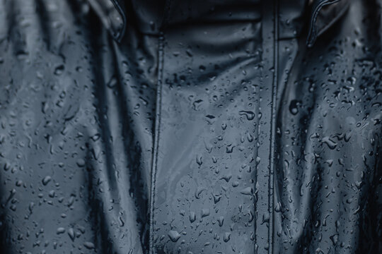 Close-up of wet dark blue waterproof raincoat with raindrops on the surface, showing texture of rain gear material.