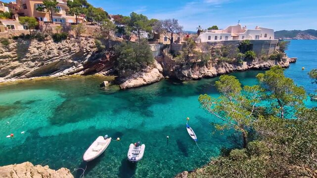 4K View of Cala de ses Llises Bay in Mallorca. Cinematic footage of Turquoise Water, Pine Trees on Rocks and Luxury Villas. Small Tropical Cove with Boats. Balearic Islands Spain.