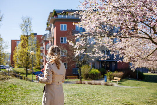 Property consultant analyzing housing options with tablet in modern neighborhood. Woman real estate agent in residential district area