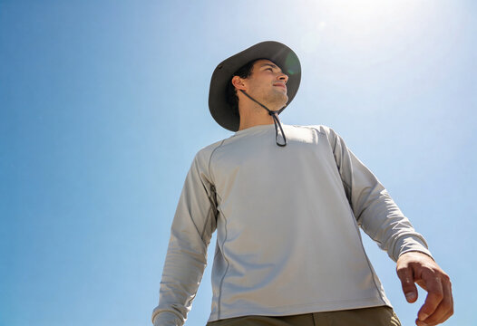 Adult man wearing a wide brim sun hat walking outdoors under a bright blue sky, summer hiking and travel lifestyle with sun protection and copy space