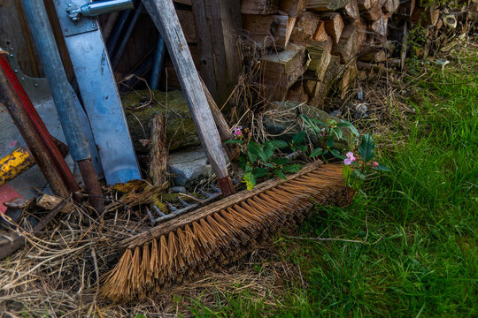 Aufnahme von einem Besen, abgestellt vor einem Holzstabel.