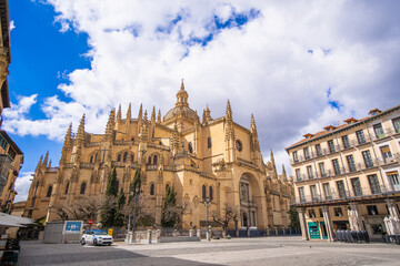 The magnificent Segovia Cathedral, Spain's last Gothic cathedral, stands proudly in the historic Plaza Mayor. Its intricate spires and detailed facade are visible under a blue sky with white clouds. © twabian