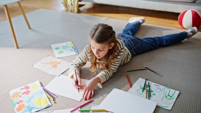 Talented child sketching lying home floor. Relaxed girl enjoying creative hobby