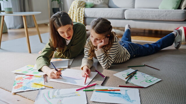 Babysitter kid creating pictures together resting floor. Mother daughter drawing