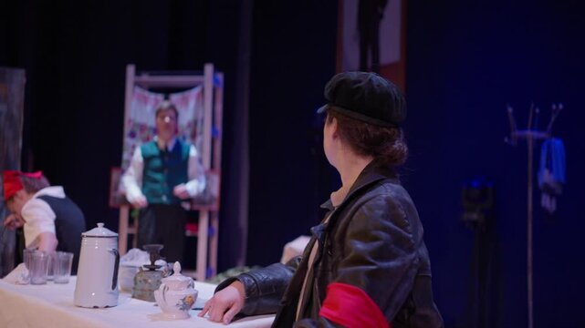 Theatrical performance with costumed actors at a table on stage, featuring vintage props, dramatic lighting, and expressive character interaction in a cozy setting