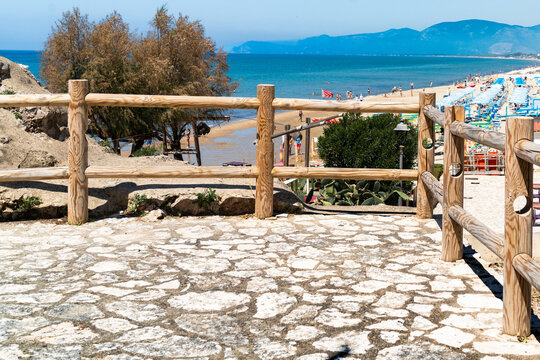 A viewing area by the sea, paved with stone slabs and fenced with a wooden turned post fence. In the background, the sea and mountains in the distance.