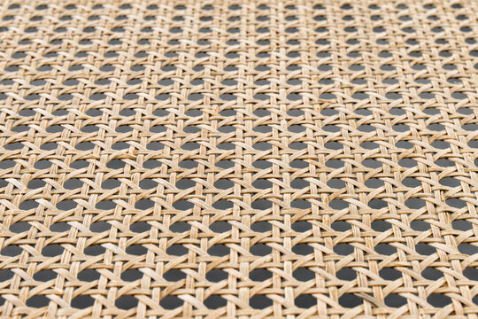 Closeup rattan weave texture showing repeating cane pattern, warm beige tones, handcrafted wicker grid, subtle shadows through open holes, visible fiber strands