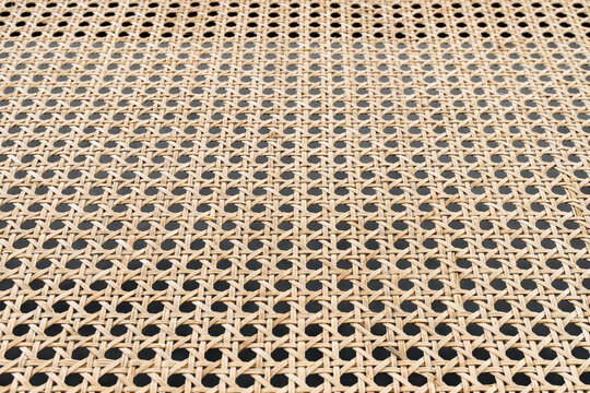 Closeup rattan weave texture showing repeating cane pattern, warm beige tones, handcrafted wicker grid, subtle shadows through open holes, visible fiber strands