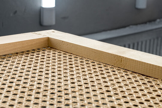 Handcrafted wooden frame with natural rattan webbing inside a professional paint booth, showcasing high-quality furniture craftsmanship and finishing