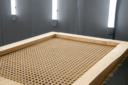 Wooden frames with stretched rattan are placed inside a spray booth for painting and finishing various wooden items. This setup is common in furniture production