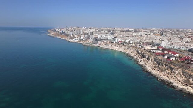 Impressive aerial drone pull away shot showcasing the Aktau city skyline stretching toward the horizon along the Caspian Sea coast. The footage highlights the famous wooden Rock Trail boardwalk