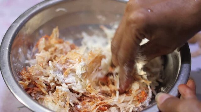 Hand mixing vibrant red chili powder and spices into shredded potatoes to create a flavorful bonda filling.