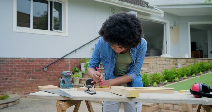 Adult woman after setup in denim measuring, marking boards at patio using sawhorse, preparing cuts