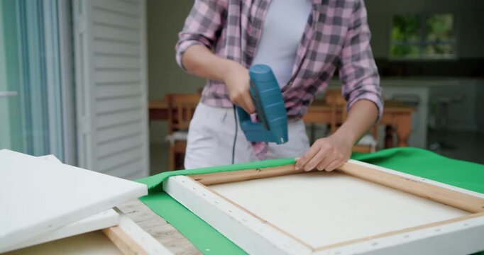 Placing frame on green fabric, African American woman pulling and stapling with blue staple gun