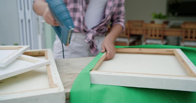 Needing decor, African American woman securing green fabric on porch with blue electric staple gun