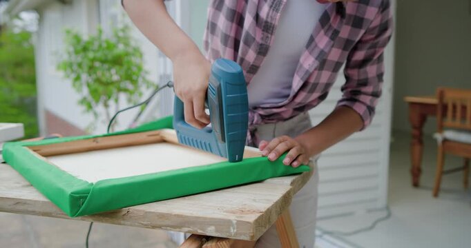Green fabric wrapped, woman pink checked shirt stapling frame, securing fabric on porch, copy space