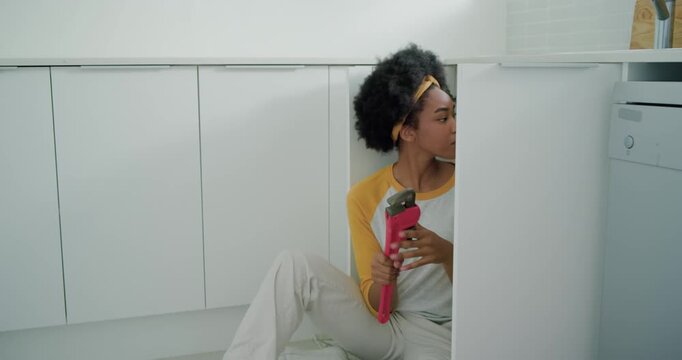 African American woman opening toolbox, grabbing pink pipe wrench and repairing P-trap under sink