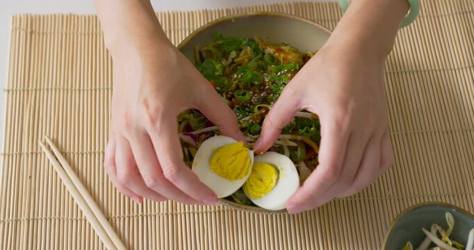 African American woman wearing mint bangle placing egg halves on salad for serving on bamboo mat