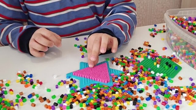 Little hands working on a bead termo-mosaic project. The child sorts and positions each piece with growing precision, hobby that encourages patience, focus, and artistic expression.