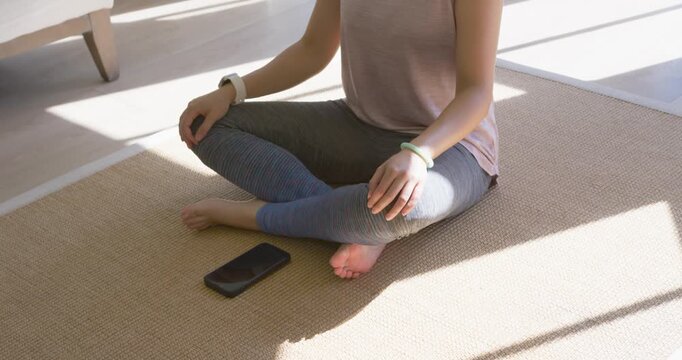 African American woman shifting then donning headphones, meditating at bay window with smartphone