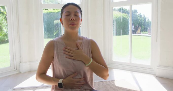 African woman sitting on mat at bay window practicing breathwork wearing earbuds and smartwatch