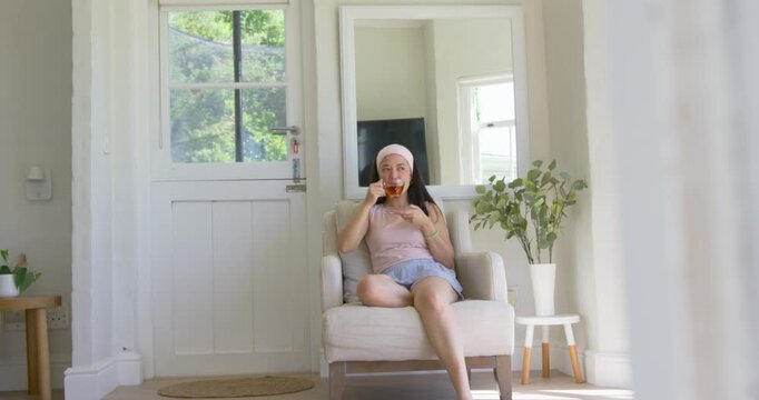Curtain moving, African American woman sitting in chair holding glass sipping tea relaxing in foyer