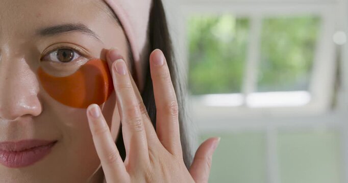 African American woman placing, smoothing crescent hydrogel patch under eye at vanity for hydration