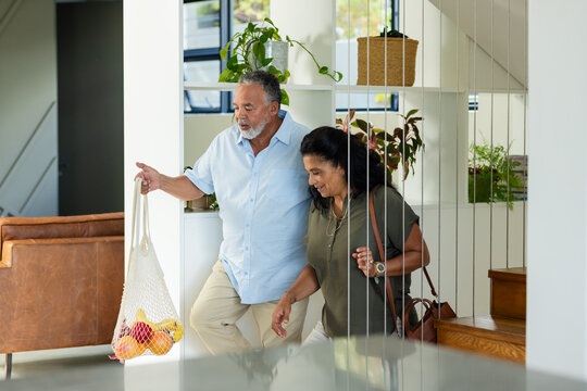 African American couple walking through bright entry carrying mesh bag with fruit and shoulder bag