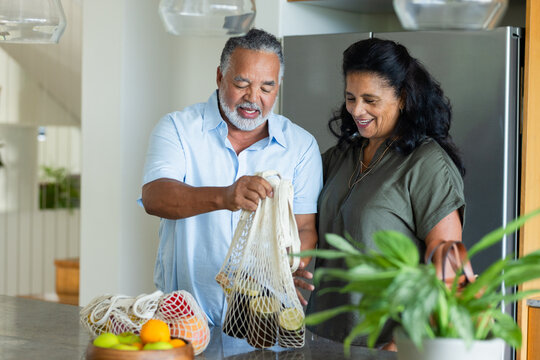 Senior African American couple unpacking groceries at kitchen counter, holding mesh produce bags