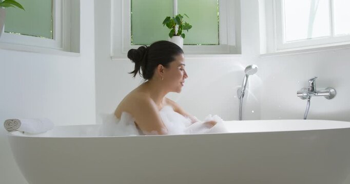 Adult female lifting, blowing foam, shaping and checking foam, moving toward hand shower in bathtub