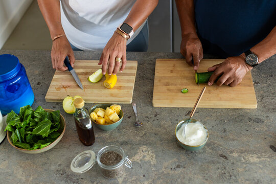 Senior African American couple slicing vegetables on wooden cutting boards at stone countertop