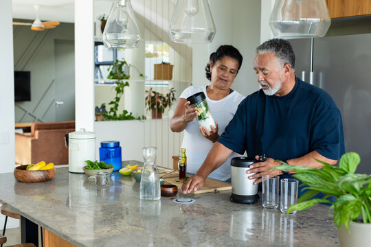African American senior couple placing blender jar on base at island, making smoothie for health