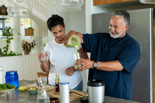 African American couple making green drink at kitchen island, man pouring blender into glass