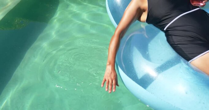 African American woman on float at pool in swimsuit skimming water and making ripples, copy space