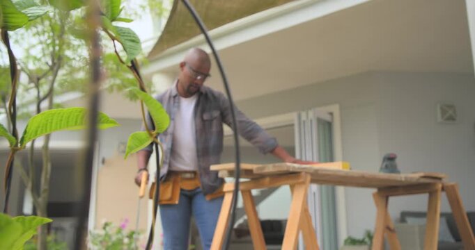 African man sawing, putting on earmuffs, measuring and sanding boards on patio for project