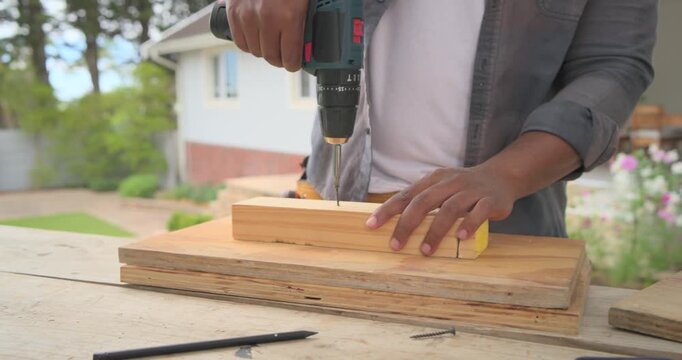 African American man placing screw, drilling block with drill to secure on porch, wearing tool belt