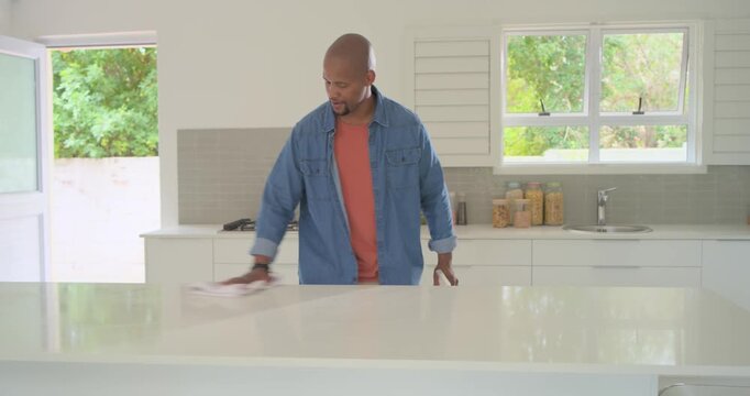 African American man seeing smudge wiping kitchen island with cloth and spray bottle ensuring clean