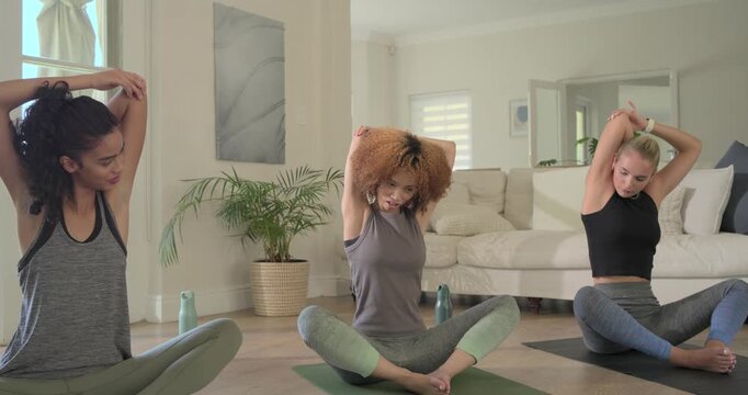 Diverse female trio in sportswear on cue stretching arms, folding forward on home mats for mobility