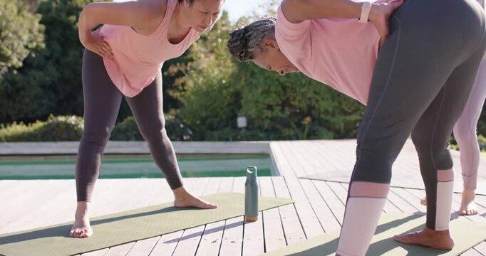 Reacting to cue, women in pink tops bending forward on deck mats while instructor guiding alignment