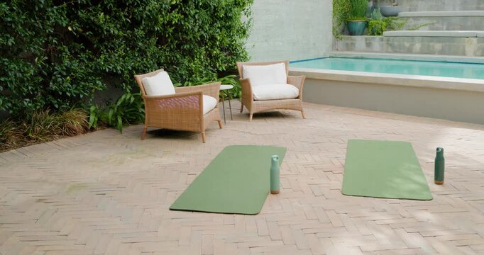Camera moving closer at poolside patio, framing green yoga mats with bottles to highlight setup
