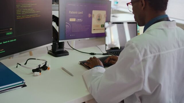 Zoom out shot of young confident Black doctor in white coat programming on computer with high tech software while conducting research in modern laboratory