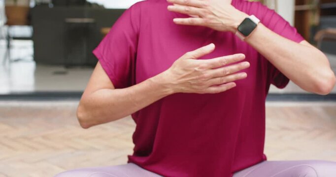 Bringing hands inward woman grounding on green patio mat, magenta top purple leggings smartwatch