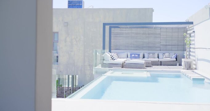 Camera panning from left, revealing rooftop pool with shallow ledge, steps, sectional sofa