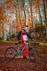 Naklejka premium Mountain biker standing with trail bike in autumn forest
