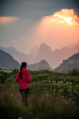 Fototapeta premium Girl in red jacket watching sunset over mountains